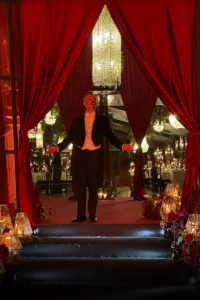 Professional Wedding MC Attilio Reinhardt in formal white tie tailcoat standing by burgundy velvet curtains at a luxury wedding entrance in Florence.